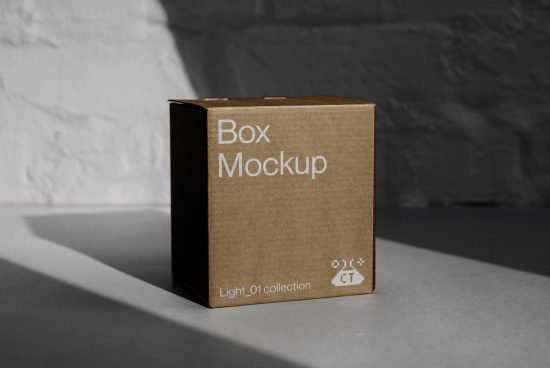 Cardboard box mockup with shadow on a grey surface against a textured wall, ideal for product packaging design presentations for designers.